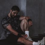 A muscular man in a gym environment taking a moment of rest, reflecting in a dark moody setting.